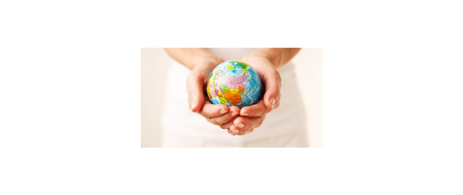 Na zdjęciu: złożone dłonie, w których trzymany jest niewielki globus 