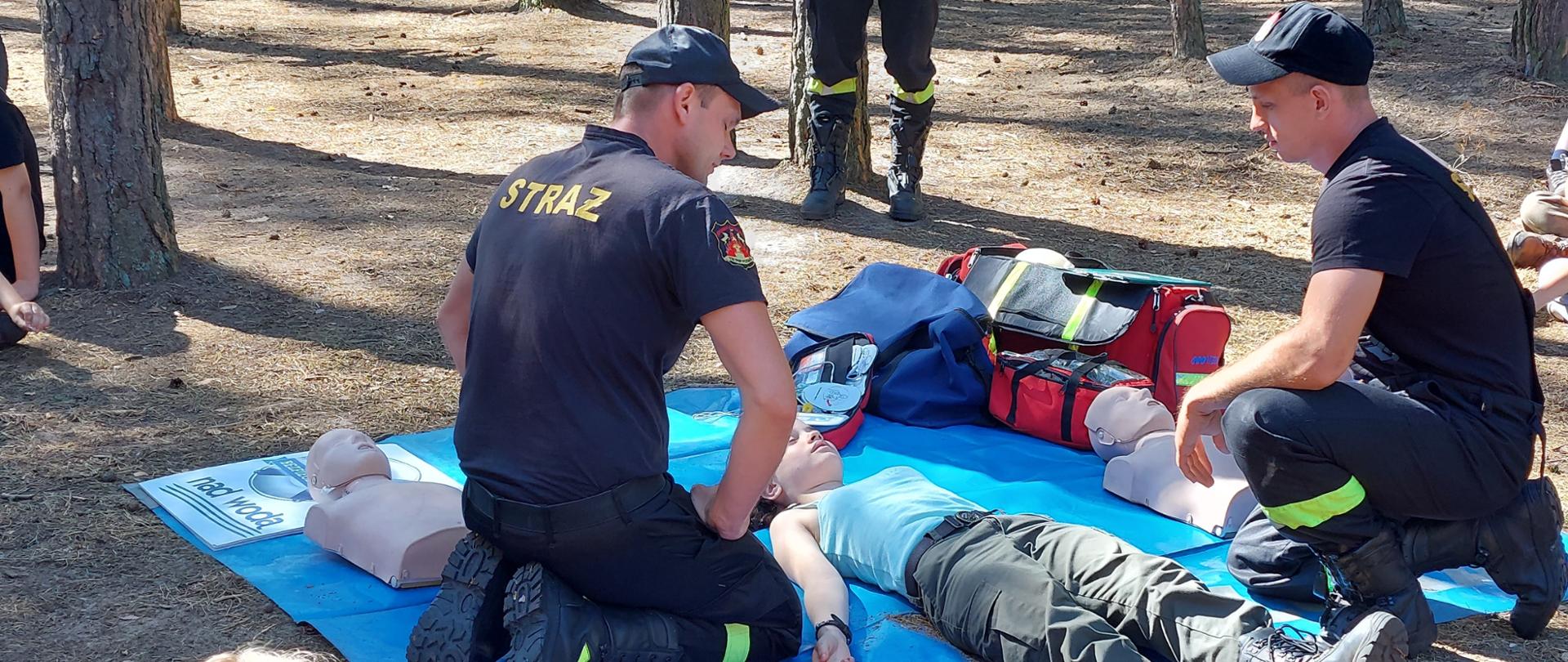 Na zdjęciu widać strażaków i harcerzy. W tle jest las.