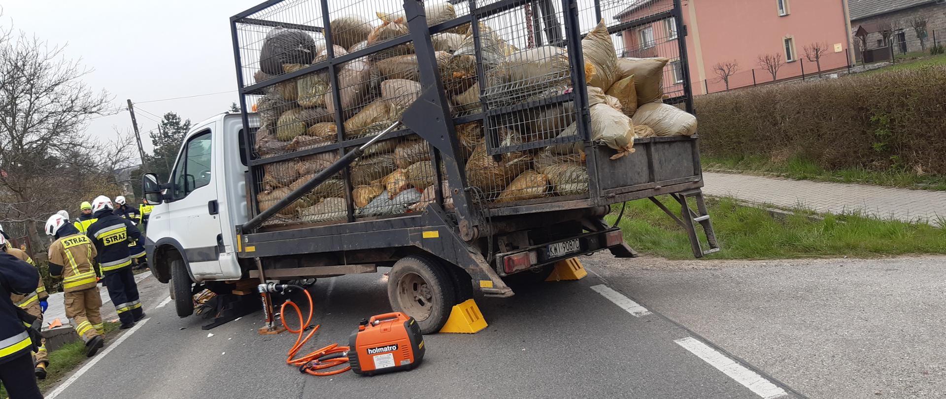 Samochód dostawczy z podniesionym bokiem przy użyciu narzędzi hydraulicznych. Obok strażacy w umundurowaniu bojowym.
