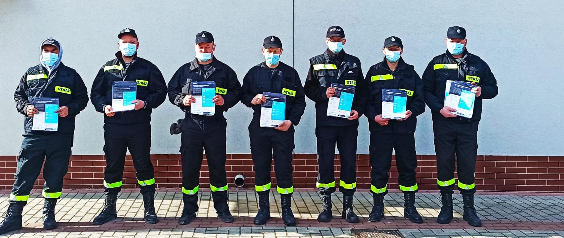 Zdjęcie przedstawia ośmiu strażaków z ulotkami w ręku na tle napisu OSP Stary Ujazd