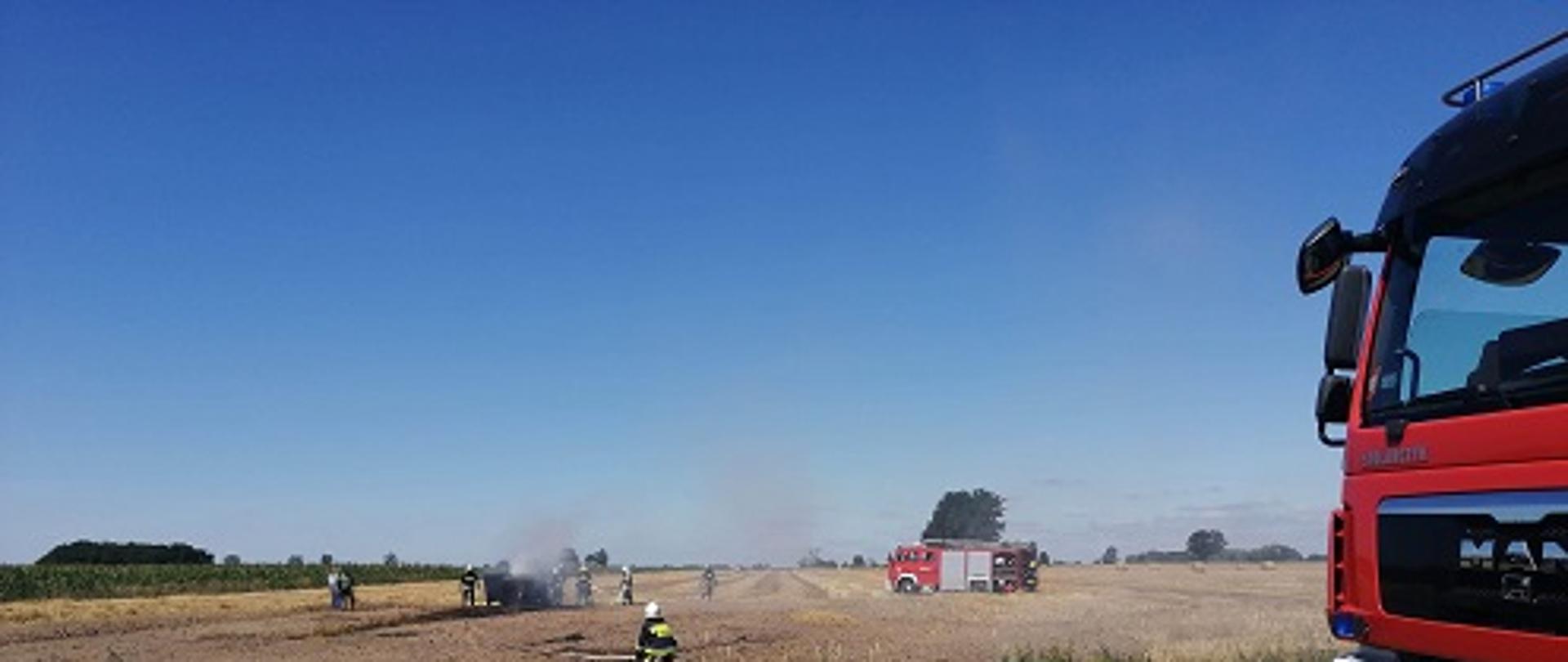 przód samochodu pożarniczego w tle strażacy gaszący pożar maszyny rolniczej