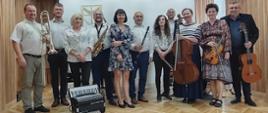 Na zdjęciu stoi na scenie grupa nauczycieli, którzy występowali na koncercie, każdy ze swoim instrumentem