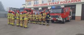 Strażacy stojąc na baczność na tle samochodów gaśniczych oddają cześć poległym strażakom z Ukrainy.
