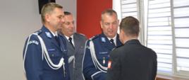 Świetlica komendy. Przedstawiciele służb mundurowych: Policji i Służby Więziennej składają komendantowi podziękowania i życzenia. Funkcjonariusze występują w umundurowaniu wyjściowym. 