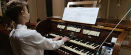 Zdjęcie przedstawia grającego organistę, widoczne nuty, kontuar organów