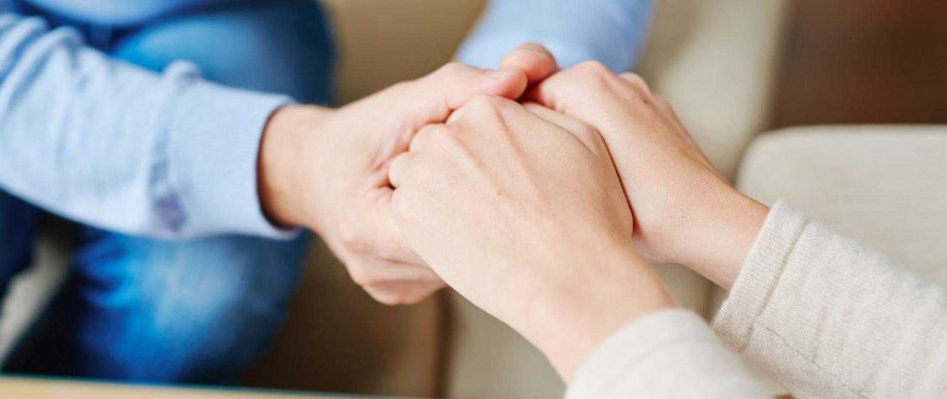 dwie osoby siedzą i trzymają się za dłonie