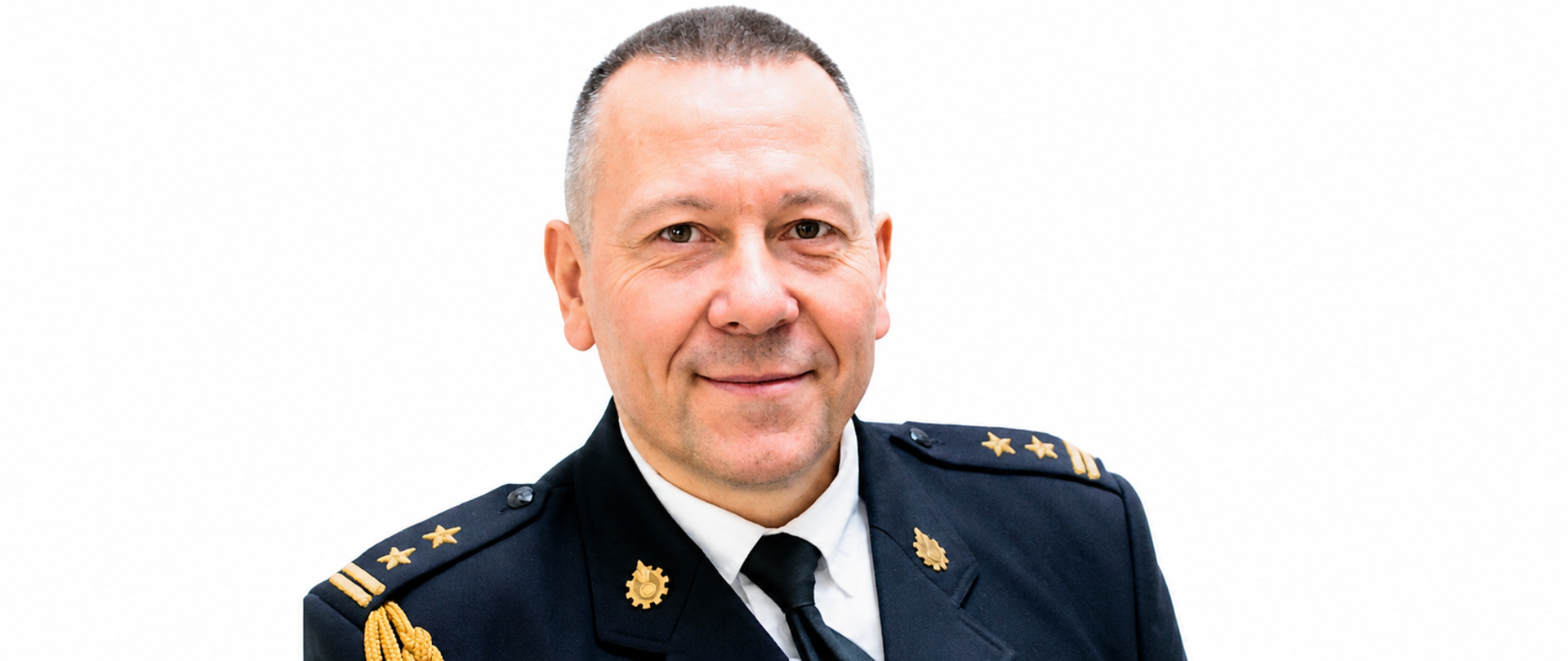 Portret Komendanta Powiatowego w mundurze strażackim na białym tle. Ma krótkie, siwe włosy i delikatny uśmiech. Na mundurze widoczne są pagony oraz odznaczenia