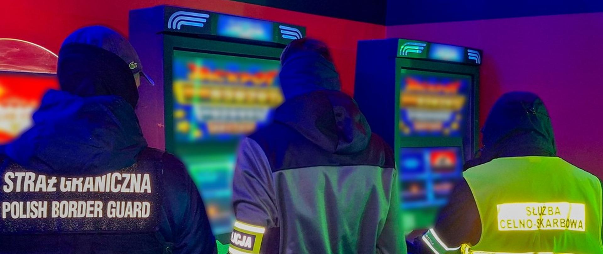 3 funkcjonariuszy we wnętrzu nielegalnego salonu gier