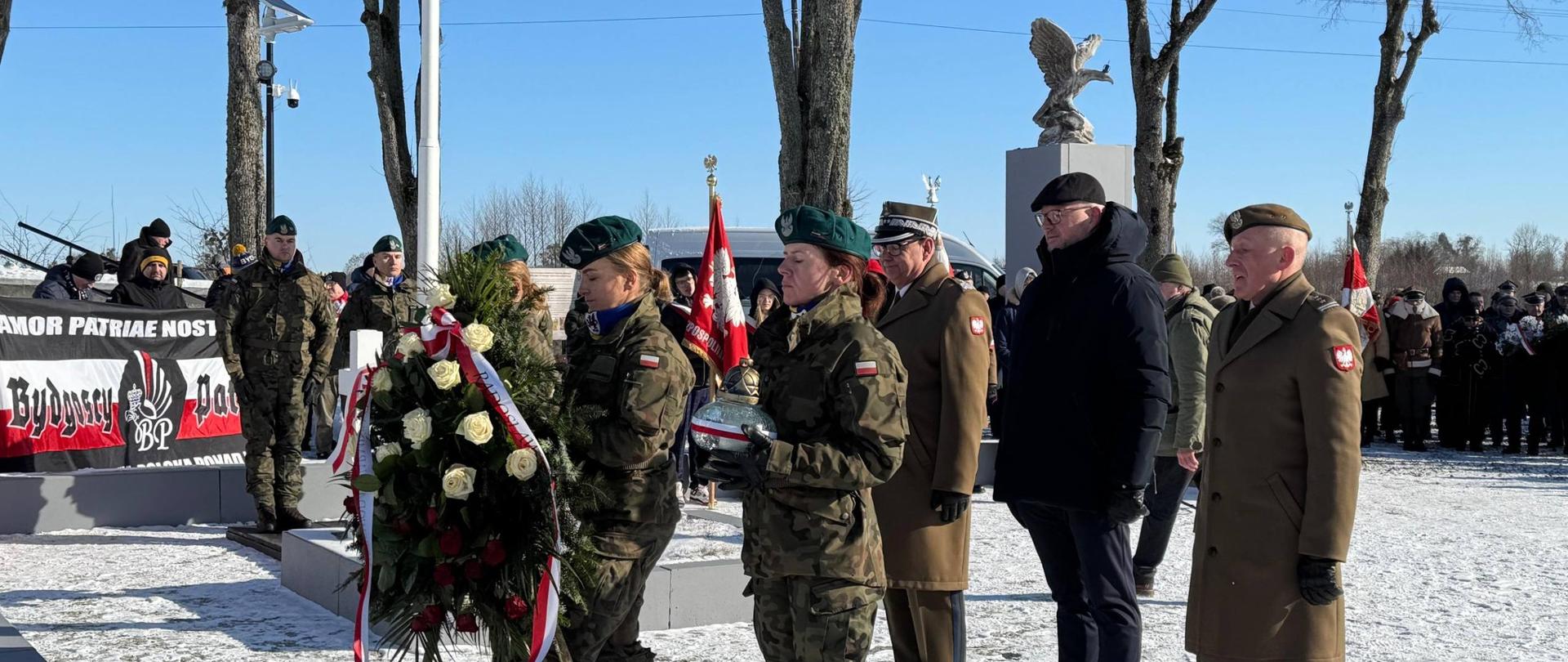 żołnierze składają kwiaty za nimi stoi mężczyzna w granatowej kurtce, wojewoda 