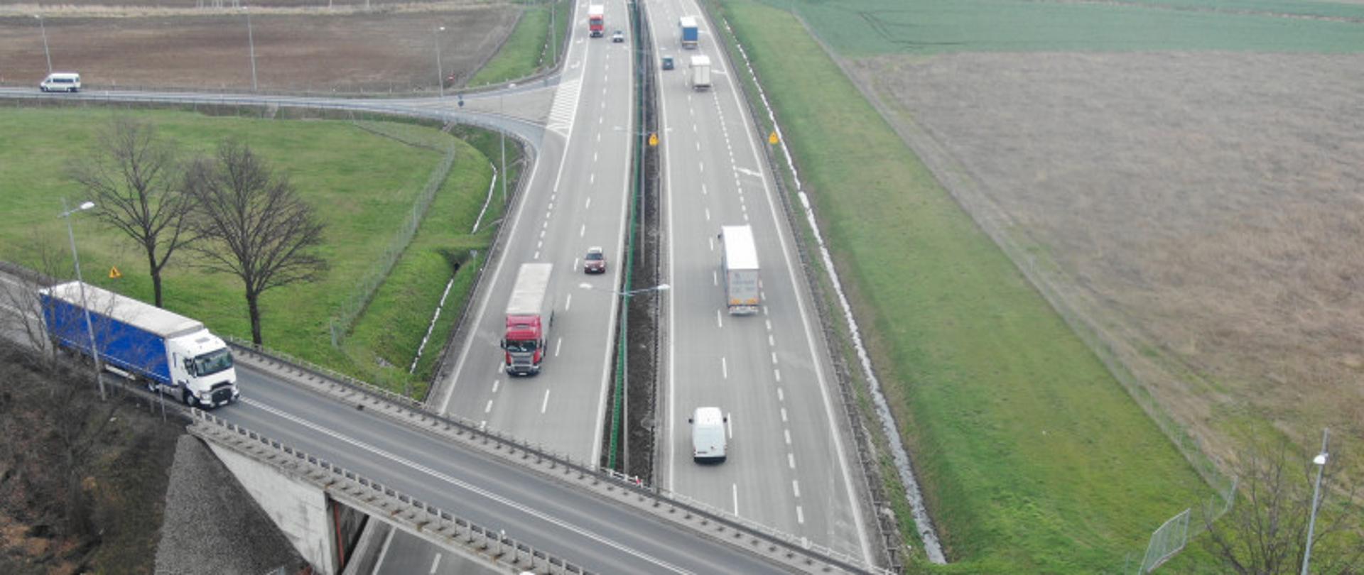 wiadukt przecina jezdnię. Widac samochodowy osobowe i ciężąrowe.