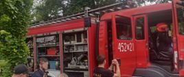 Na zdjeciu widoczny jest wóz strażacki podczas festynu którego oglądaja mieszkańcy widać w nim sprzęt hydrauliczny, weże strażackie. Widać zainteresowanych mieszkańców którzy ogladaja wóz oraz sródek kabiny wozu.