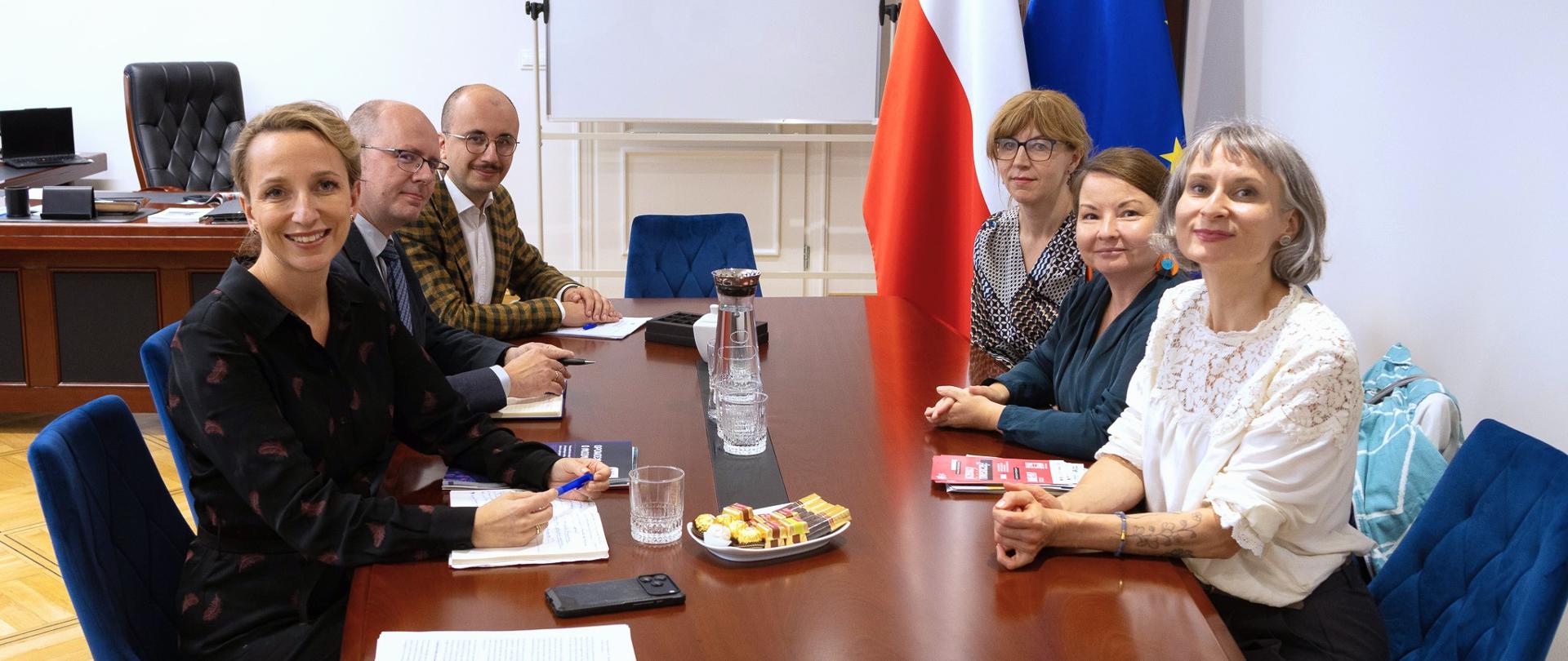 Sześć osób siedzi przy stole w gabinecie RPO i uśmiecha się pozując do zdjęcia