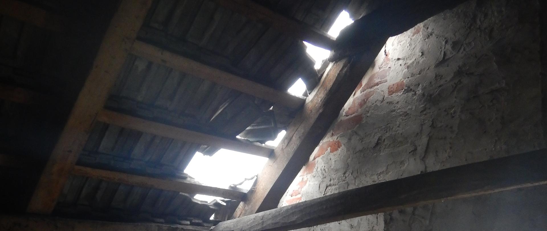 Zdjęcie przedstawia uszkodzone elementy poszycia dachowego. Zdjęcie wykonano z wnętrza obiektu.