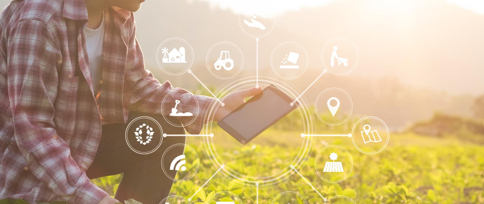Gospodarstwo rolne, na którym przebywa mężczyzna. W lewej ręce trzyma tablet. Wokół tabletu rozmieszczone są ikony, które symbolizują funkcje lub aplikacje, które mogą ułatwić rolnikom pracę