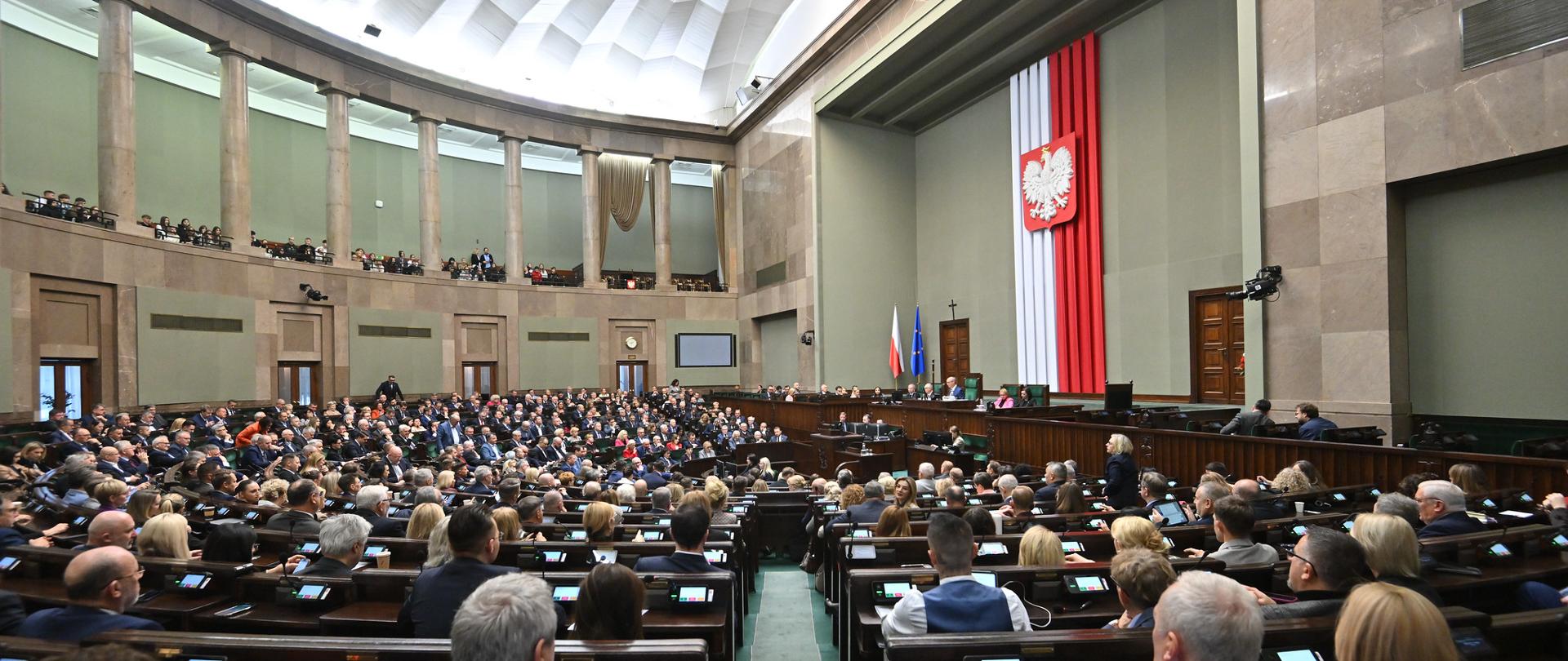 Posiedzenie Sejmu podczas którego przyjęto ustawę wdrażającą CBAM, czyli Mechanizm Dostosowywania Cen na Granicach z Uwzględnieniem Emisji CO2. To tarcza dla polskiego przemysłu. Na zdjęciu widać posłów w ławach sejmowych głosujących. 