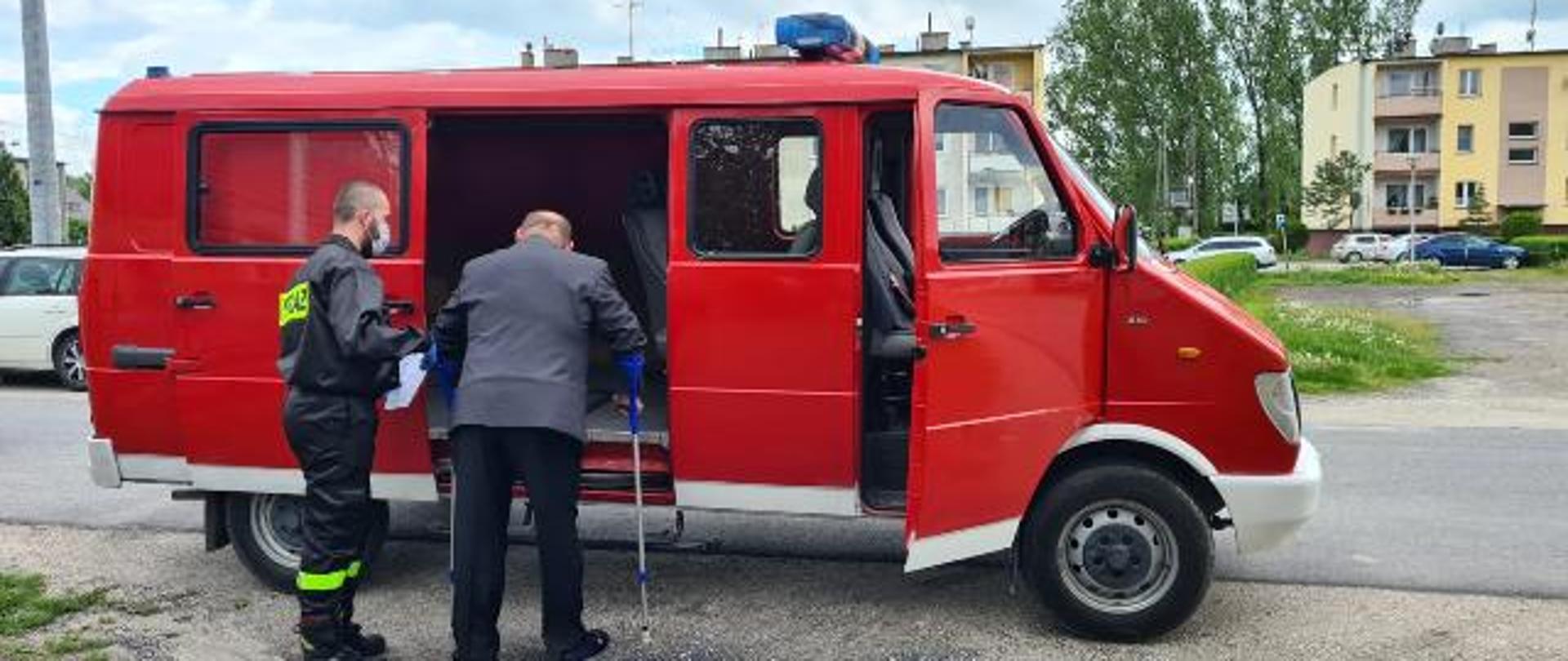 zdjęcie przedstawia strażaka ochotnika pomagającego starszemu Panu wejść do samochodu 