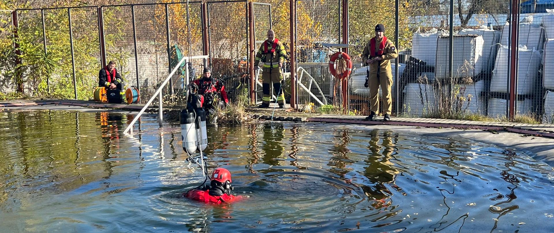 Strażak nurek w zbiorniku wodnym, czterech innych strażaków na brzegu