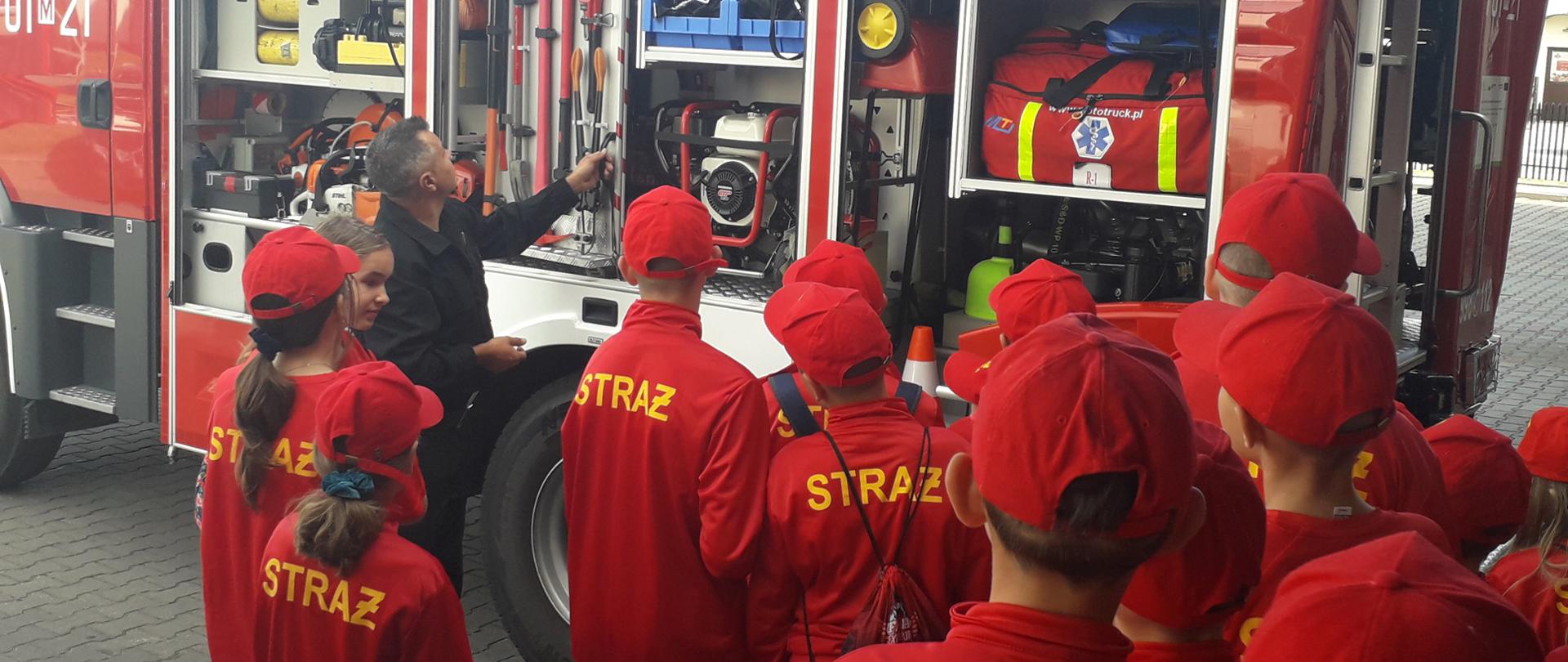 Pokaz sprzętu, młodzieżowa drużyna obserwuje strażaka pokazującego sprzęt na samochodzie