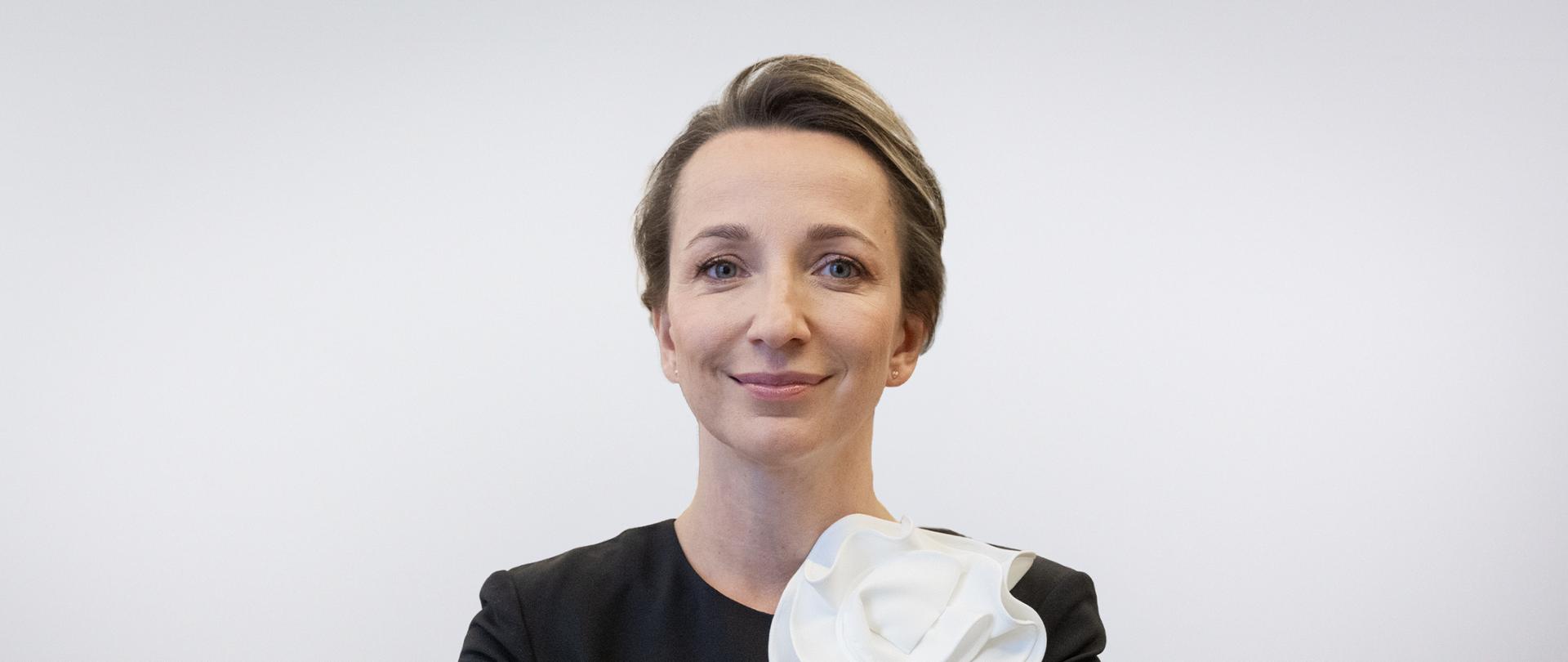 Portret Sylwii Gregorczyk-Abram - uśmiechnięta kobieta w sukience z założonymi rękoma