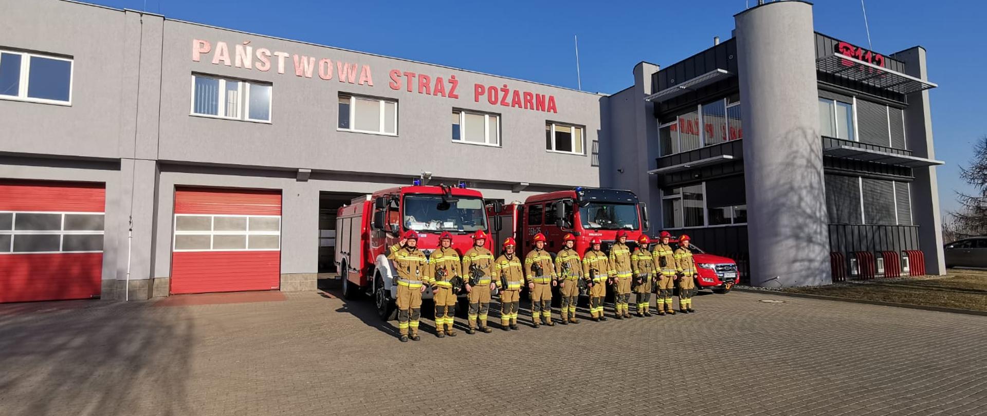 Na zdjęciu widać strażaków którzy oddali hołd poległym strażakom z Ukrainy. Strażacy stoją przed remizą i przed samochodami. 