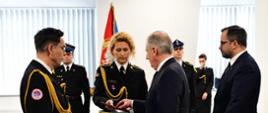 Wojewoda pomorski oraz sekretarz stanu w Ministerstwie Infrastruktury wręczają medal strażakowi zakładowej służby ratowniczej. Medal podaje strażaka.