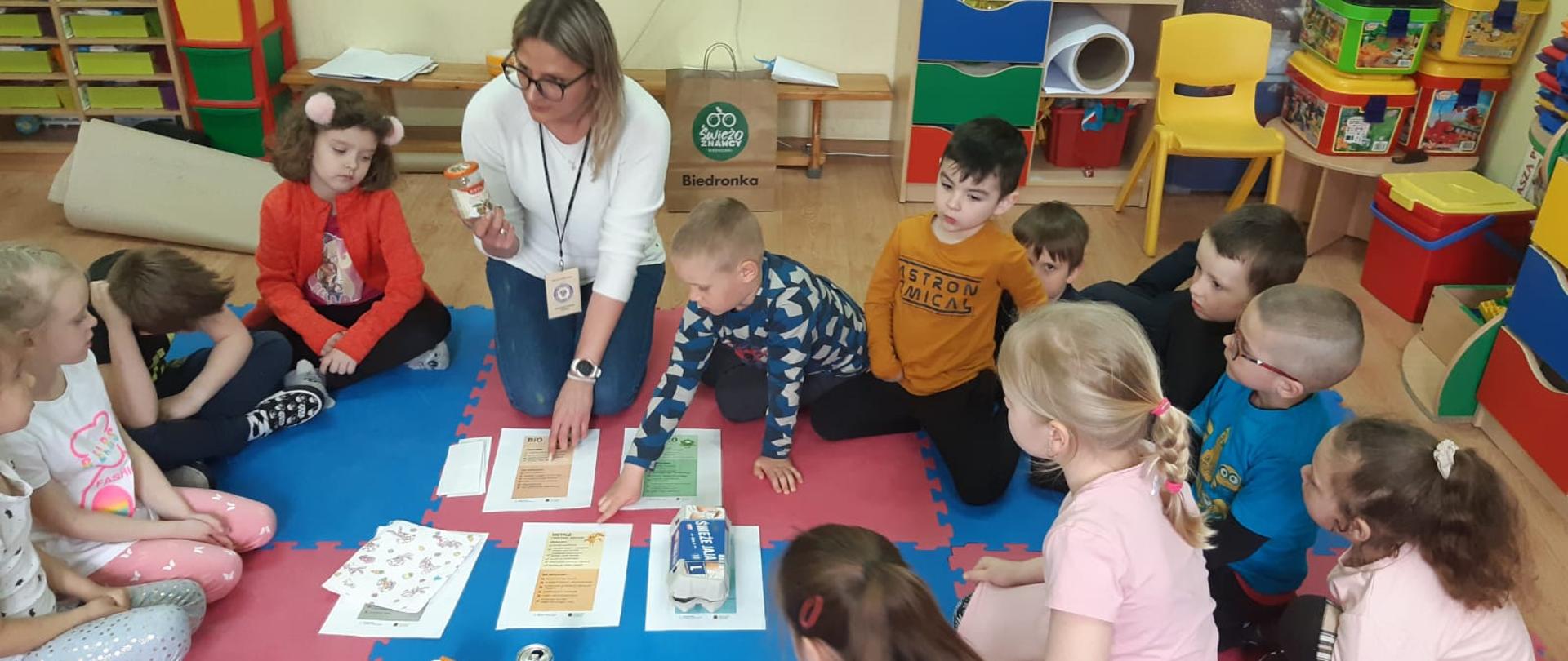 Zdjęcie przedstawia obchodzi Światowego dnia zdrowie 2022. Pracownik Inspekcji Sanitarnej pokazuje dzieciom w przedszkolu jak prawidłowo segregować odpady