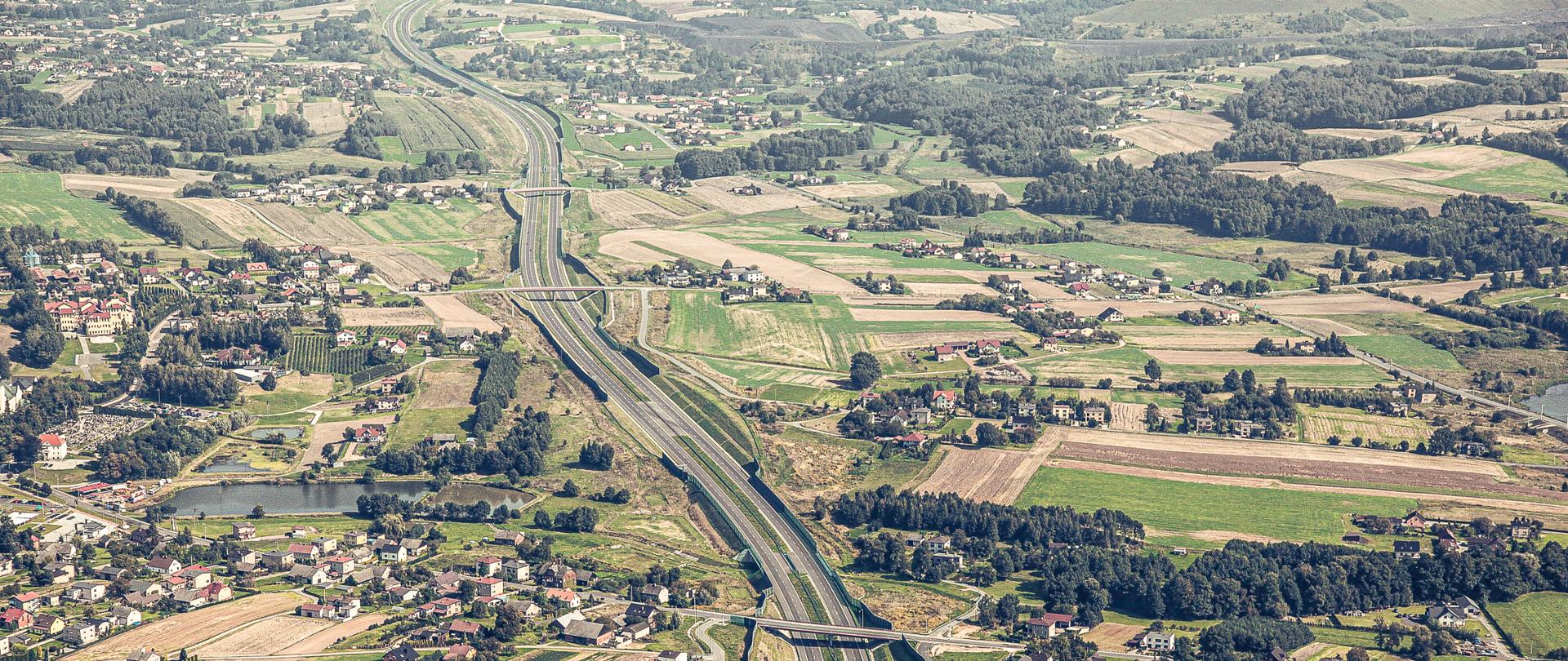 Fotografia wykonana z lotu ptaka przedstawia autostradę przecinającą wertykalnie słabo zurbanizowane tereny z licznymi wiaduktami nad autostradą komunikujące położone przy autostradzie zabudowania. Autostrada przebiega w większości w wykopie, Wyposażona w liczne ekrany akustyczne. Obszar wzdłuż autostrady mieszany. Występują na nim tereny rolnicze, zalesione oraz niewielkie skupiska zabudowy jednorodzinnej.
