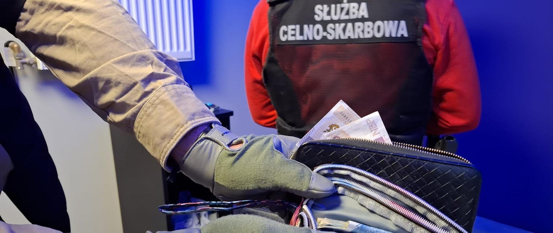 Funkcjonariusz KAS pokazuje zawartość saszetki, w której znajduje się duża ilość gotówki.