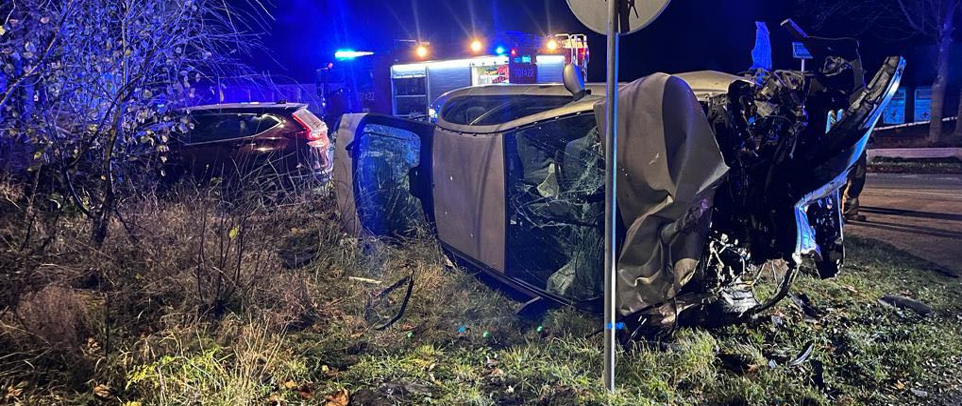 Zderzenie dwóch aut, jedno leży na boku, drugie wpadło w krzaki
