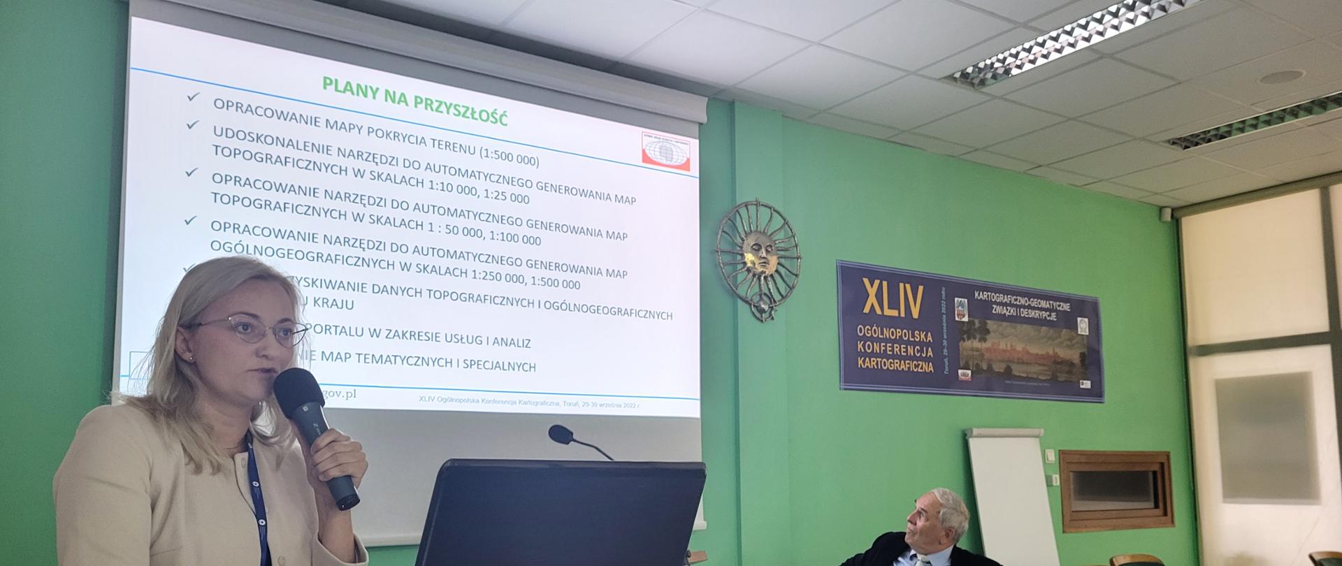 Zdjęcie przedstawia Annę Bober, Dyrektor Departamentu Geodezji, Kartografii i Systemów Informacji Geograficznej w trakcie wygłaszanego w imieniu p.o. GGK referatu dot. działań GGK w obszarze kartografii.