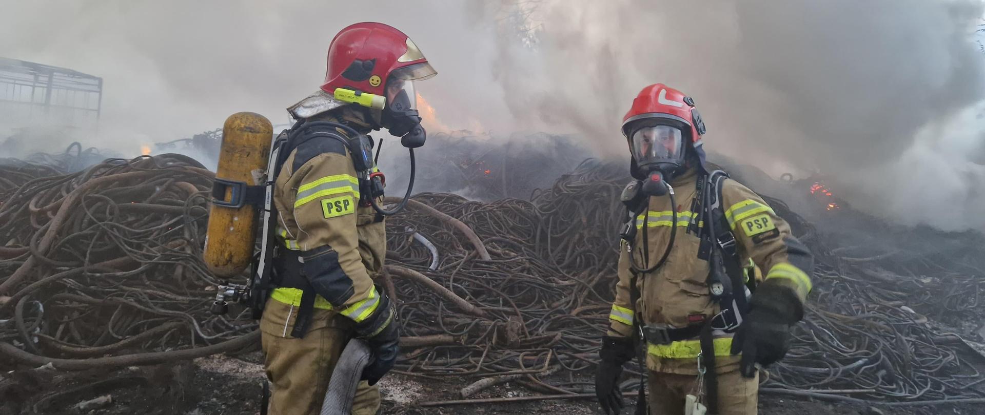 Pożar składowiska odpadów, przed którym stoją strażacy przygotowani do działań.