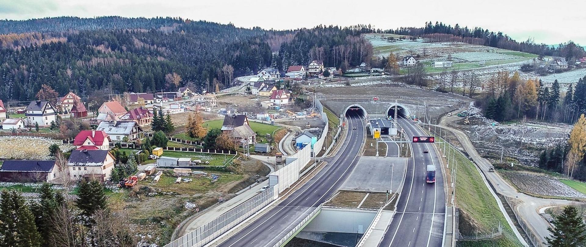 droga ekspresowa w terenie górskim, wjazd do tunelu, w tle góry i zabudowa jednorodzinna