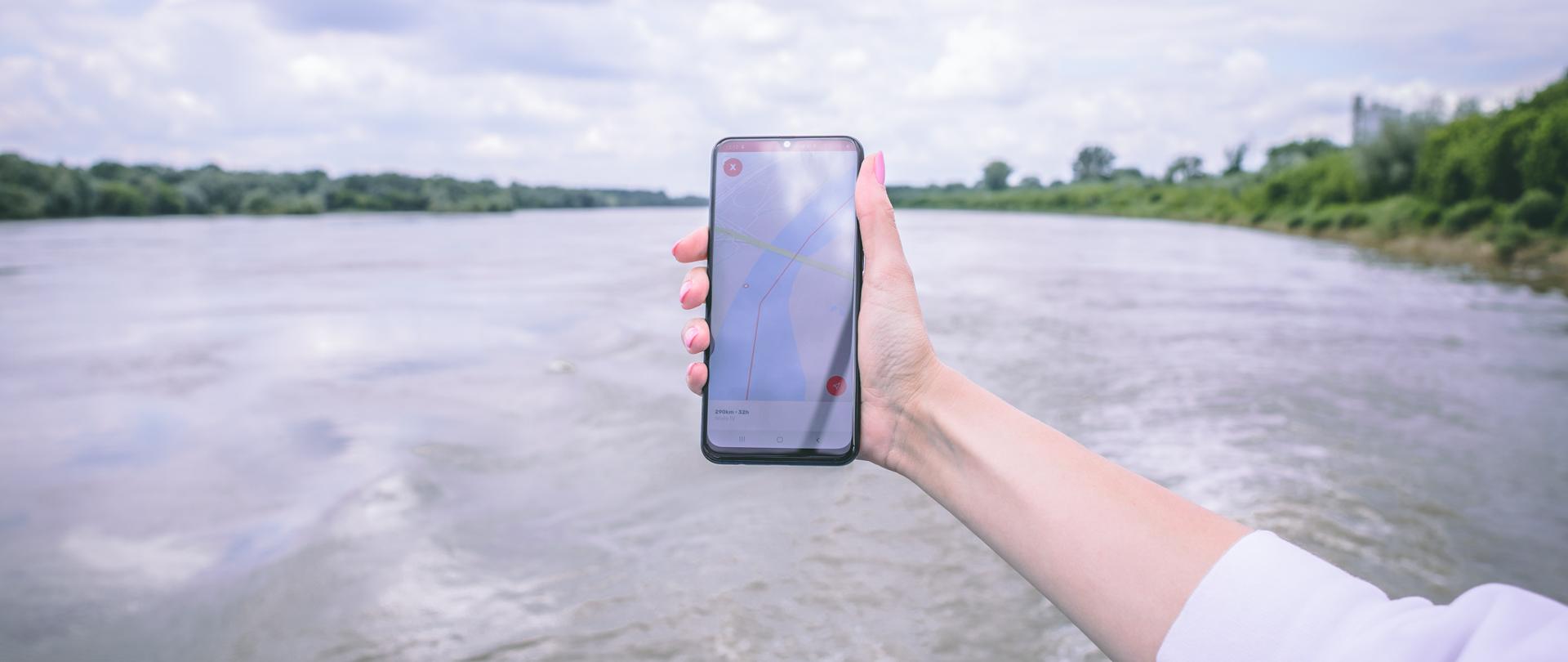 Telefon z otwartą aplikacja na tle rzeki