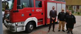 Strażak Państwowej Straży Pożarnej przedstawiciel gminy oraz druhowie ochotniczej straży pożarnej stoją obok samochodu gaśniczego.