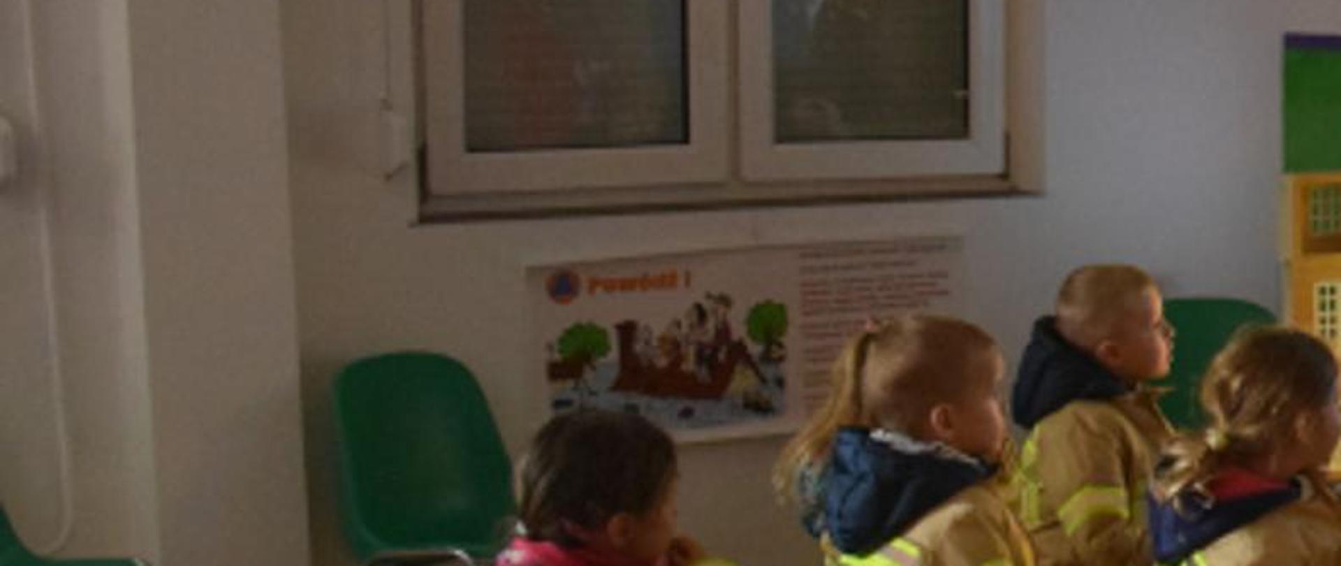 Na zdjęciu grupa przedszkolaków oraz strażak prezentujący Symulator Zagrożeń Pożarowych 