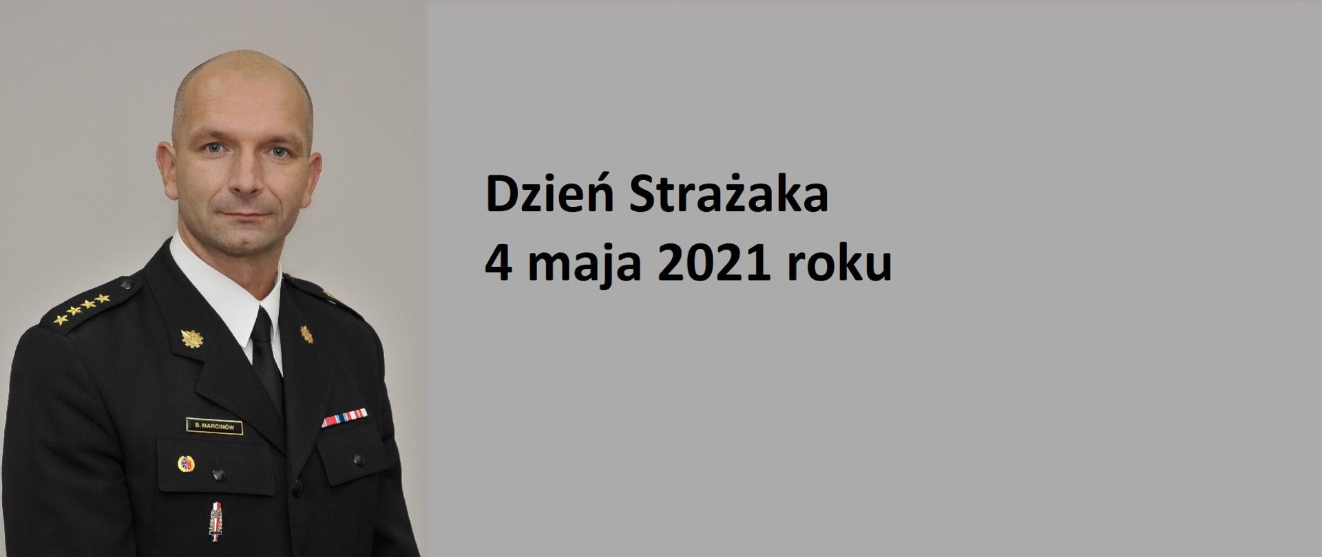 Na zdjęciu widać Komendanta Bartłomieja Marcinów w mundurze wyjściowym oraz napis Dzień Strażaka, 4 maja 2021 roku