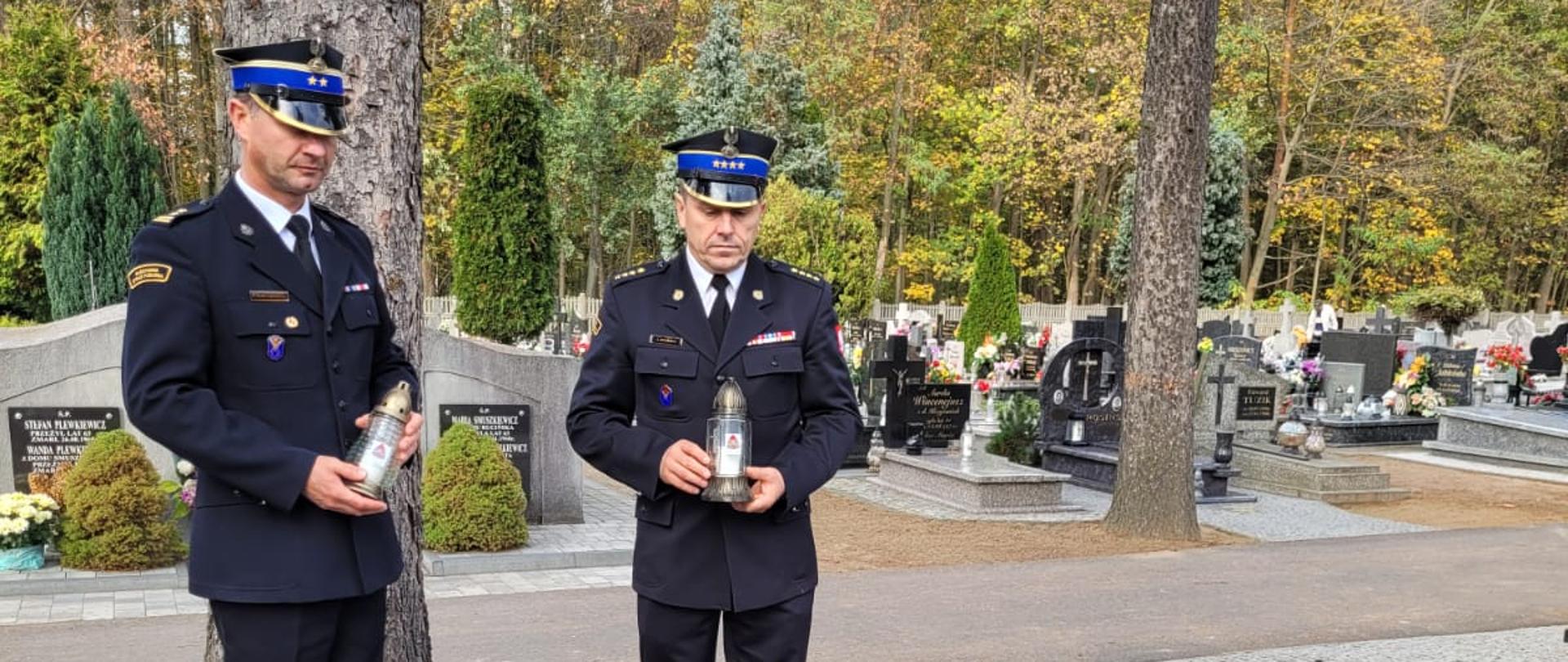 strażacy trzymają w rekach znicze nad grobem zmarłego strażaka