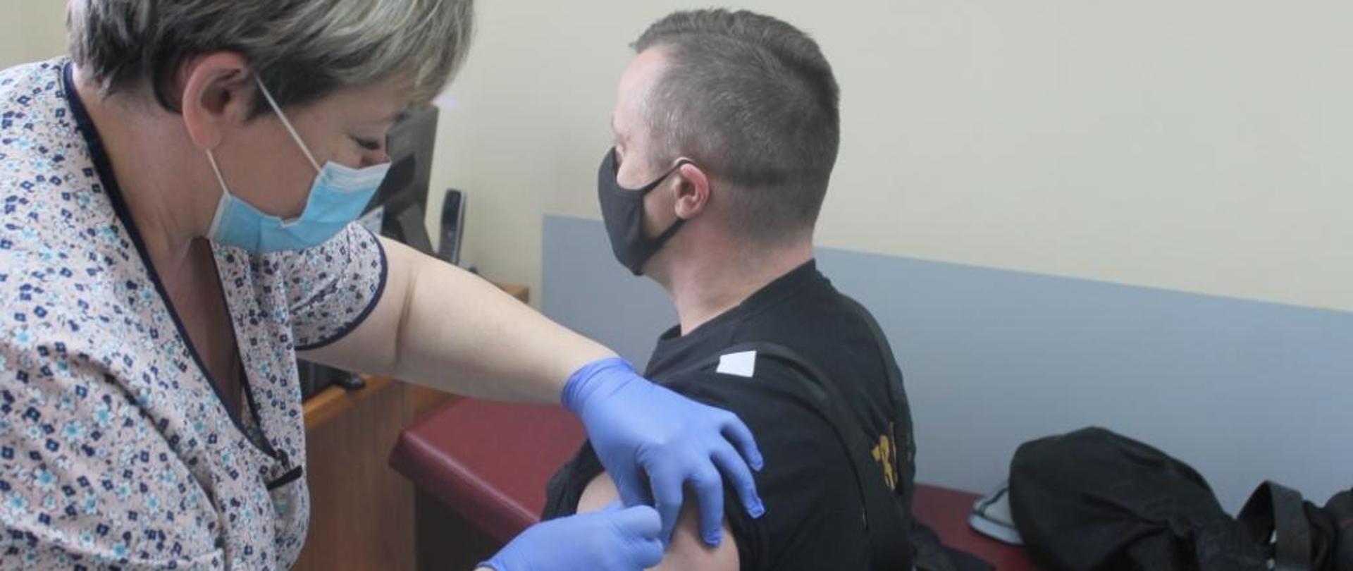 Zdjęcie przedstawia strażaka PSP podczas szczepienia przeciw COVID-19