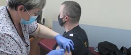 Zdjęcie przedstawia strażaka PSP podczas szczepienia przeciw COVID-19