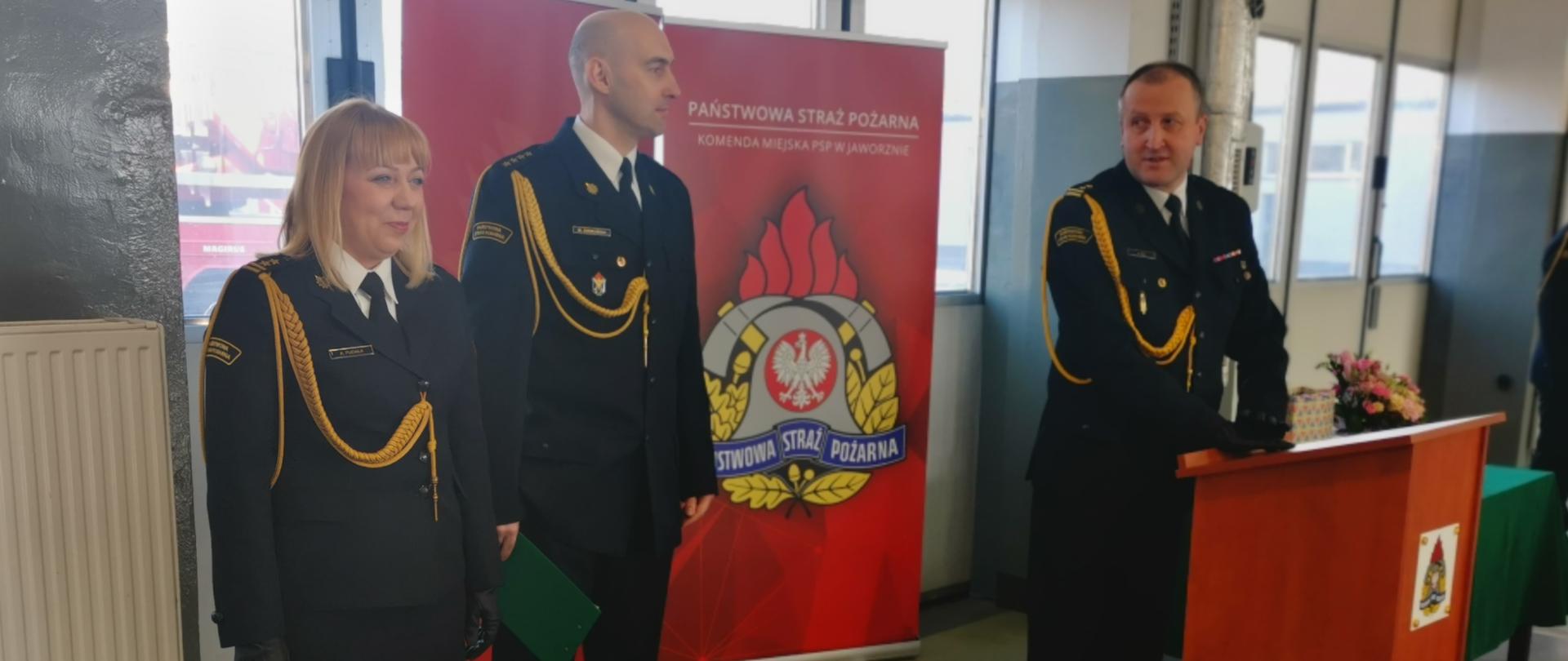 Na zdjęciu widoczna bryg. Anna fudała, st.kpt. Marcin Ziemiański oraz bryg.Paweł Żaba w mundurach wyjściowych na garażu JRG Jaworzno.
