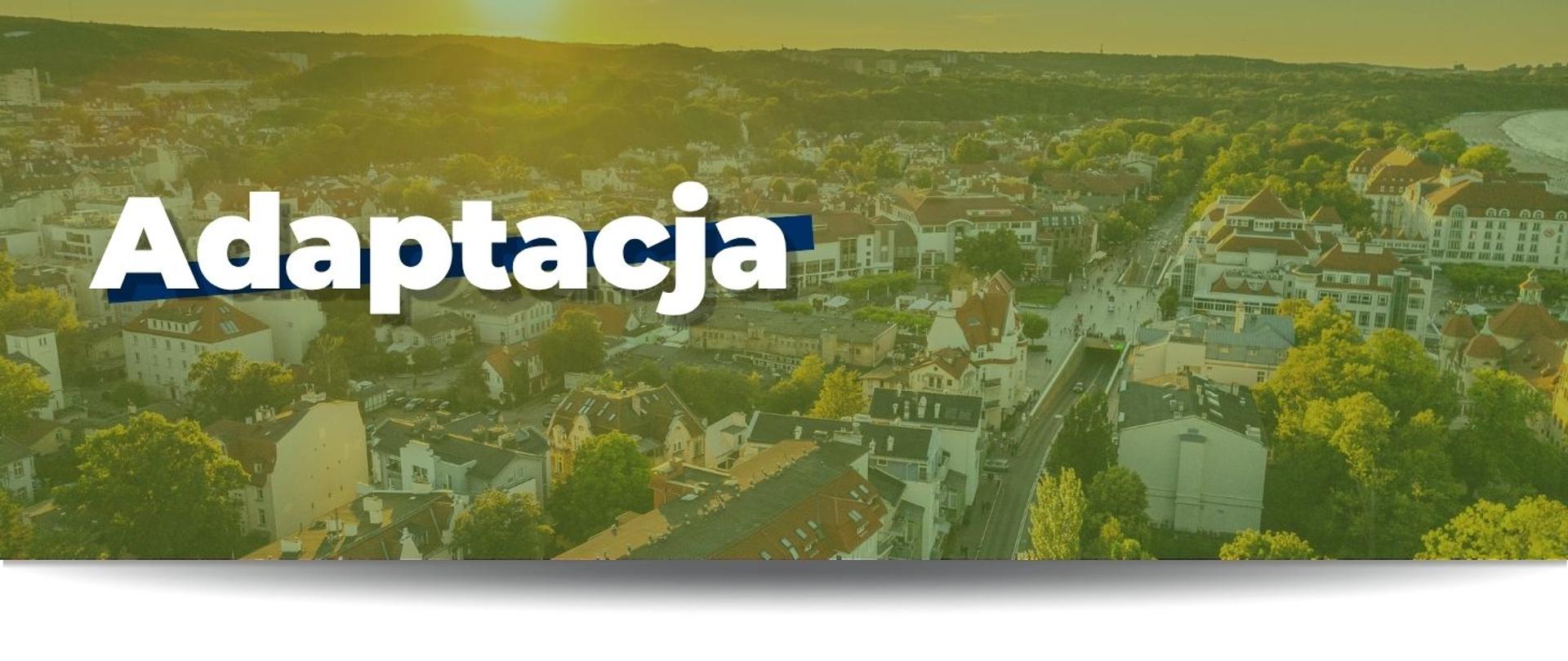 Na grafice widnieje biały napis "Adaptacja". W tle widać zdjęcie przedstawiające nadmorskie miasto. Na grafice widać budynki, ulice, skrawek plaży a w tle lasy.