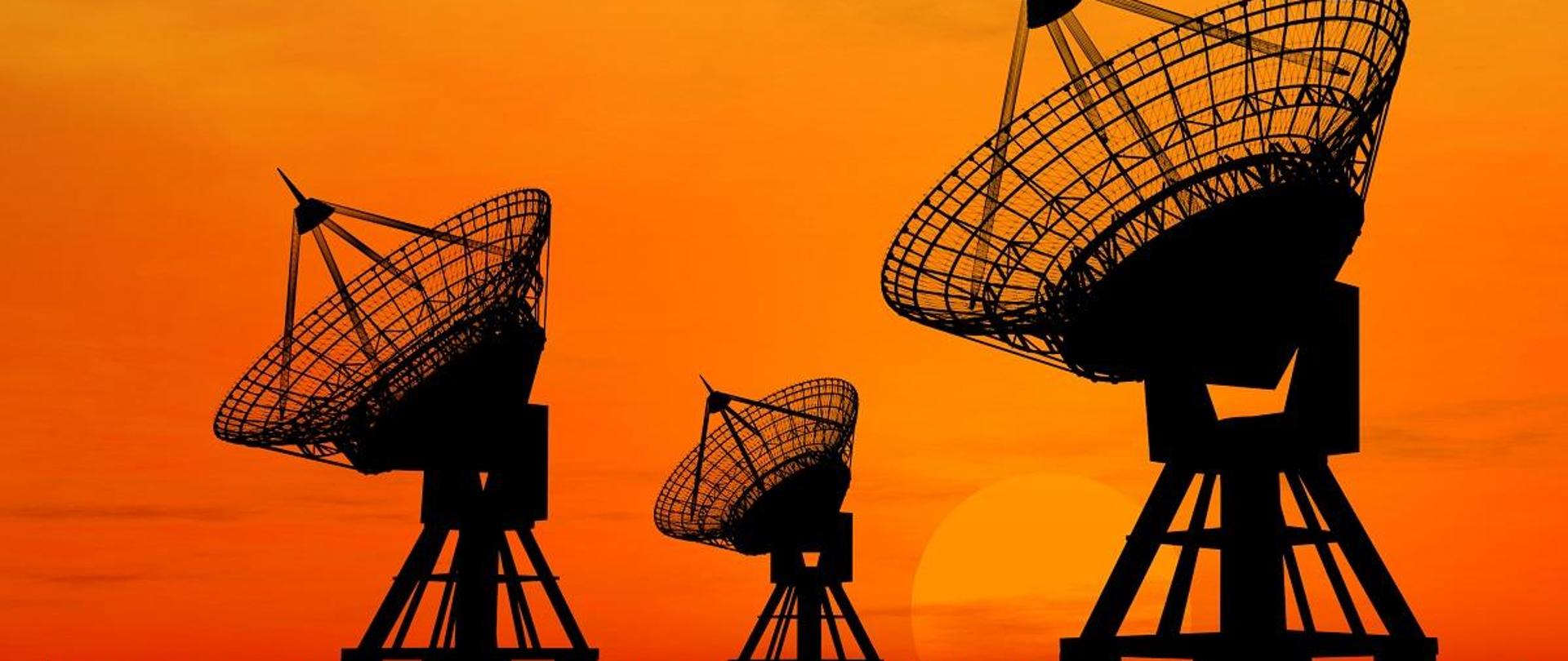 Radioteleskopy na tle pomarańczowego nieba i zachodzącego Słońca