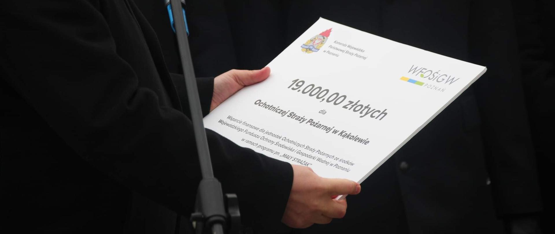 Osoba trzyma tabliczkę z napisami obok stoi mikrofon.