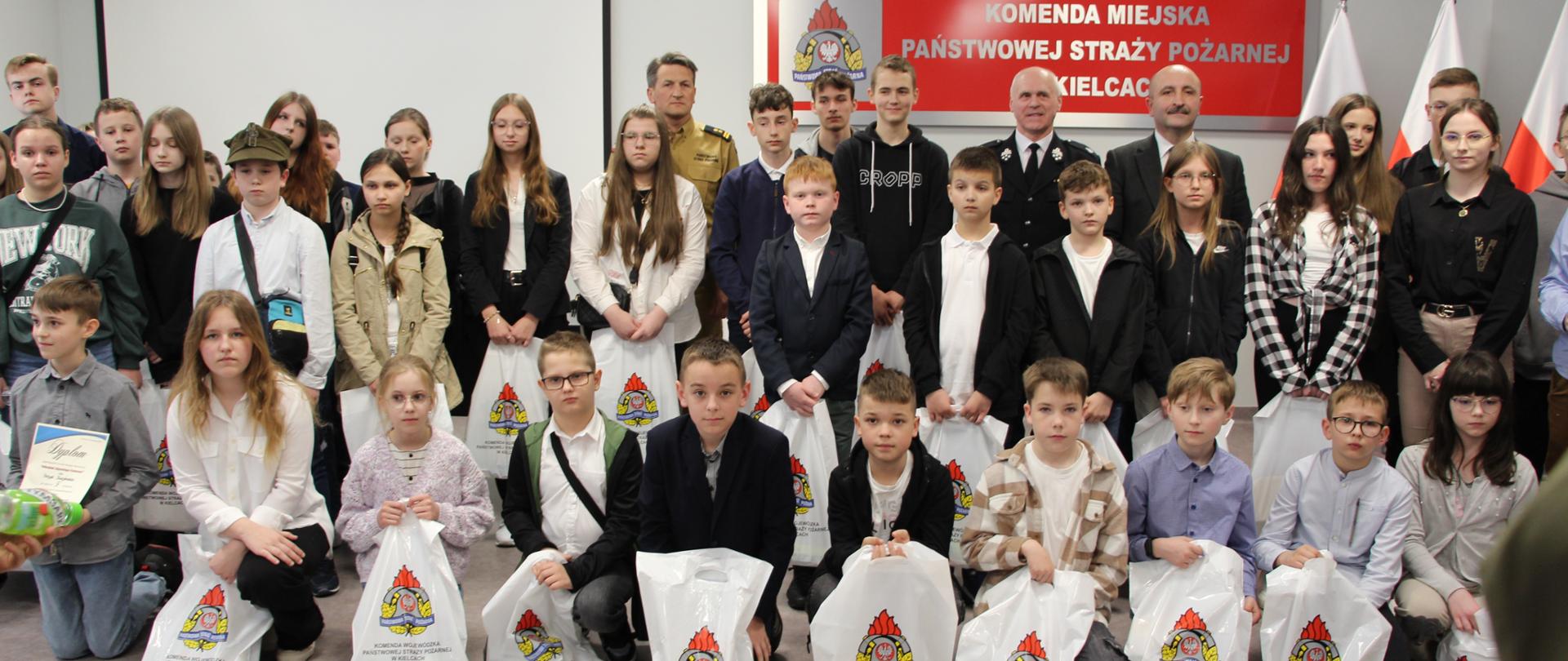 Zdjęcie przedstawia wszystkich uczestników eliminacji powiatowych OTWP wraz z Komendantem Miejskim PSP w Kielcach bryg Mariuszem Górą, Członkiem Zarządu Starostwa Powiatowego Mariuszem Ściana i prezesem Zarządu Powiatowego OSP Ireneuszem Żakiem