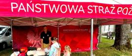 Zdjęcie przedstawia stoisko PSP na dożynkach. Przy stoisku stoi strażak oraz zainteresowane osoby. 