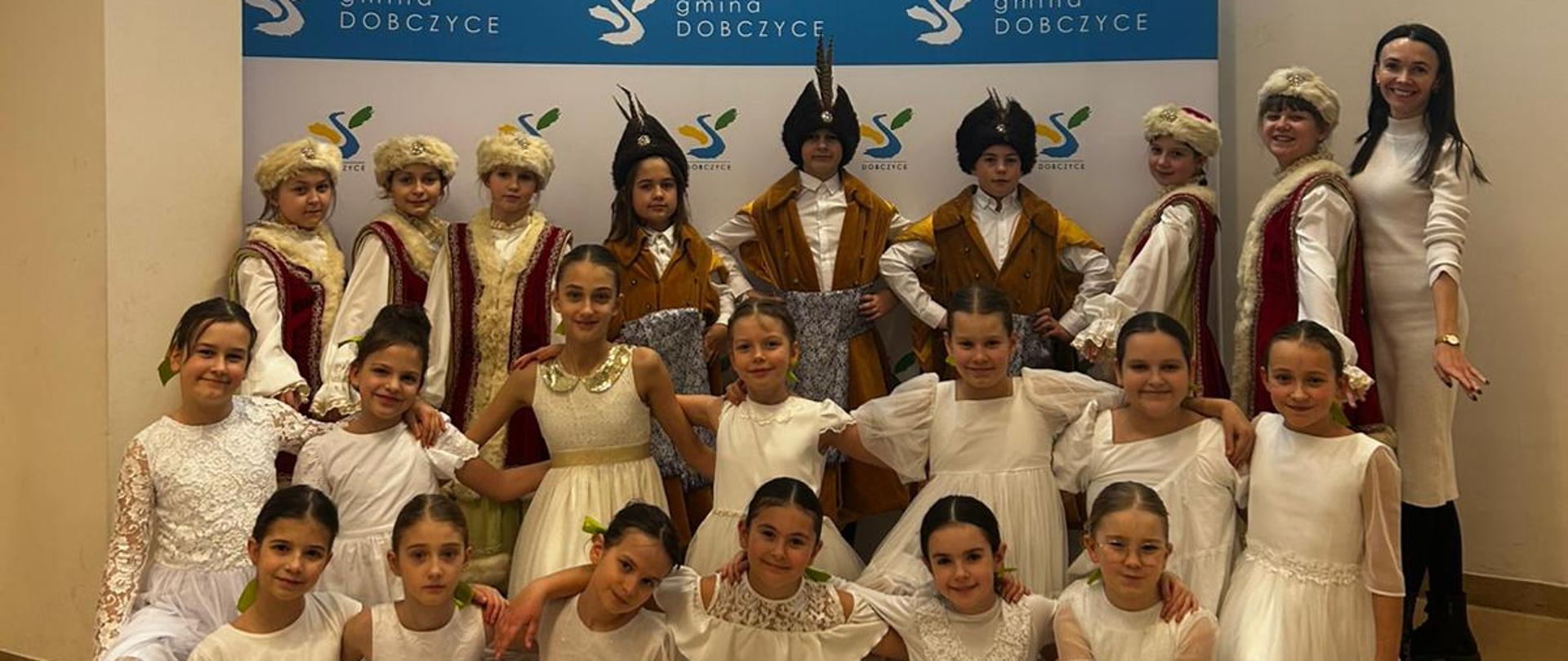 Grupa dzieci w strojach tanecznych pozuje do wspólnego zdjęcia po występie artystycznym podczas festiwalu zespołów rytmicznych.