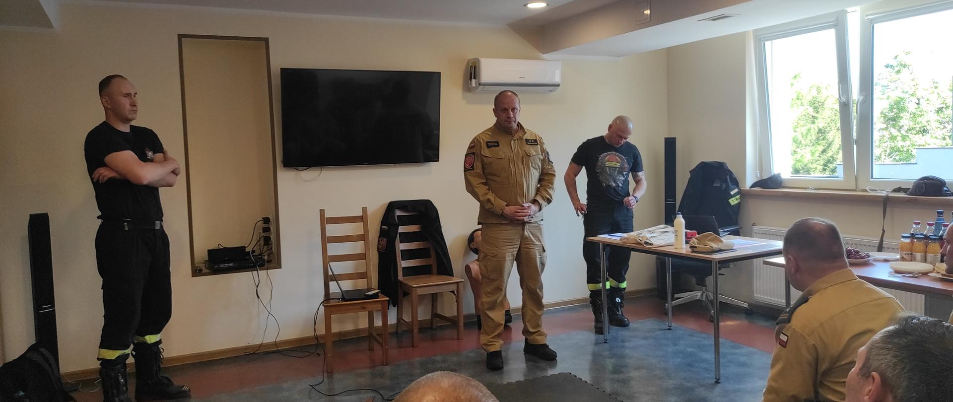 Zdjęcie zrobione w pomieszczeniu świetlicy. Na zdjęciu trzech strażaków z komisji egzaminacyjnej.