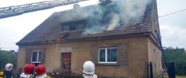 Zdjęcie przedstawia strażaków gaszących pożar domu.
W tle budynek.
