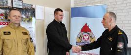 Zdjęcie przedstawia trzech strażaków w biurze Komendanta Powiatowego PSP podczas przywitania po odbytym szkoleniu.