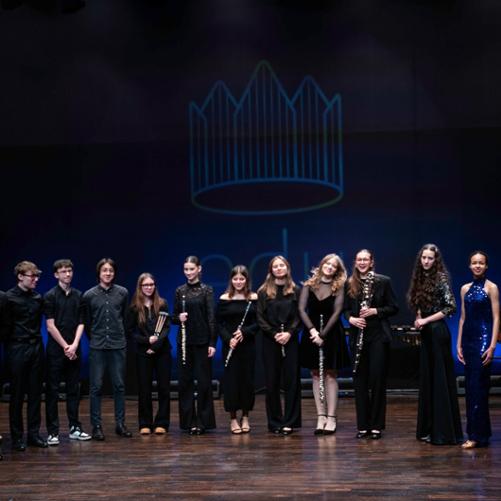 zdjęcie przedstawia wszystkich uczestników koncertu we wspólnym zdjęciu z instrumentami na scenie sali koncertowej